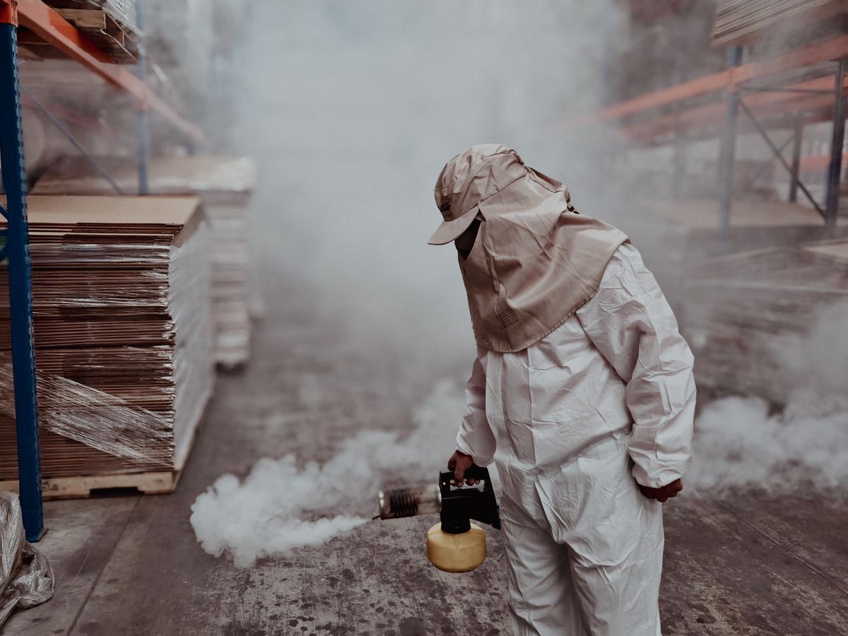 Pest control technician in protective gear fogging a commercial warehouse aisle